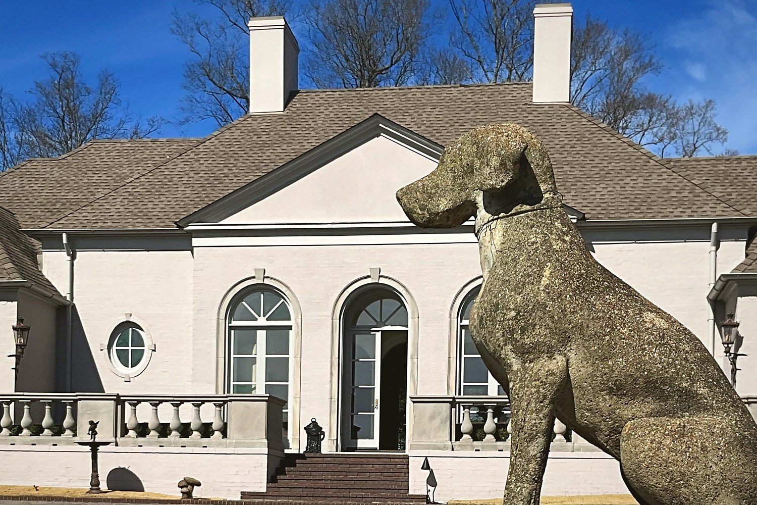 A stately Alabama home with a weathered stone hound sculpture on the gate pier